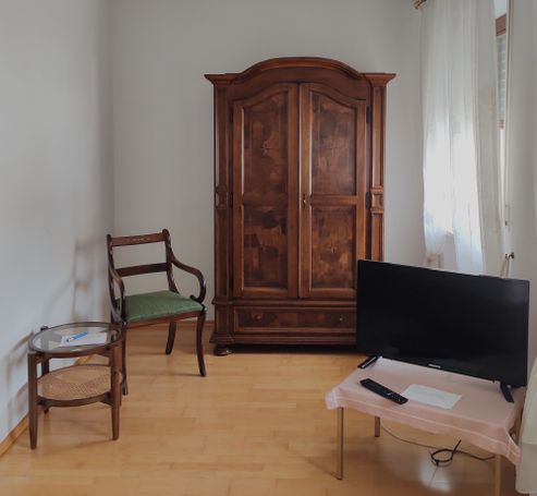 Schrank, Stuhl mit rundem Beistelltisch, TV auf rechteckigem Tischchen.